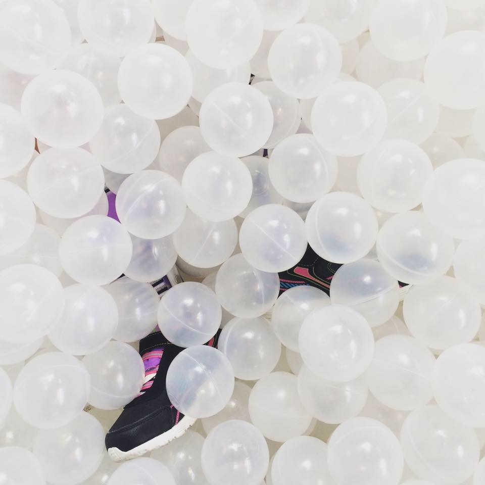 ball pit filled with white balls with 2 black and pink sneakers poking out